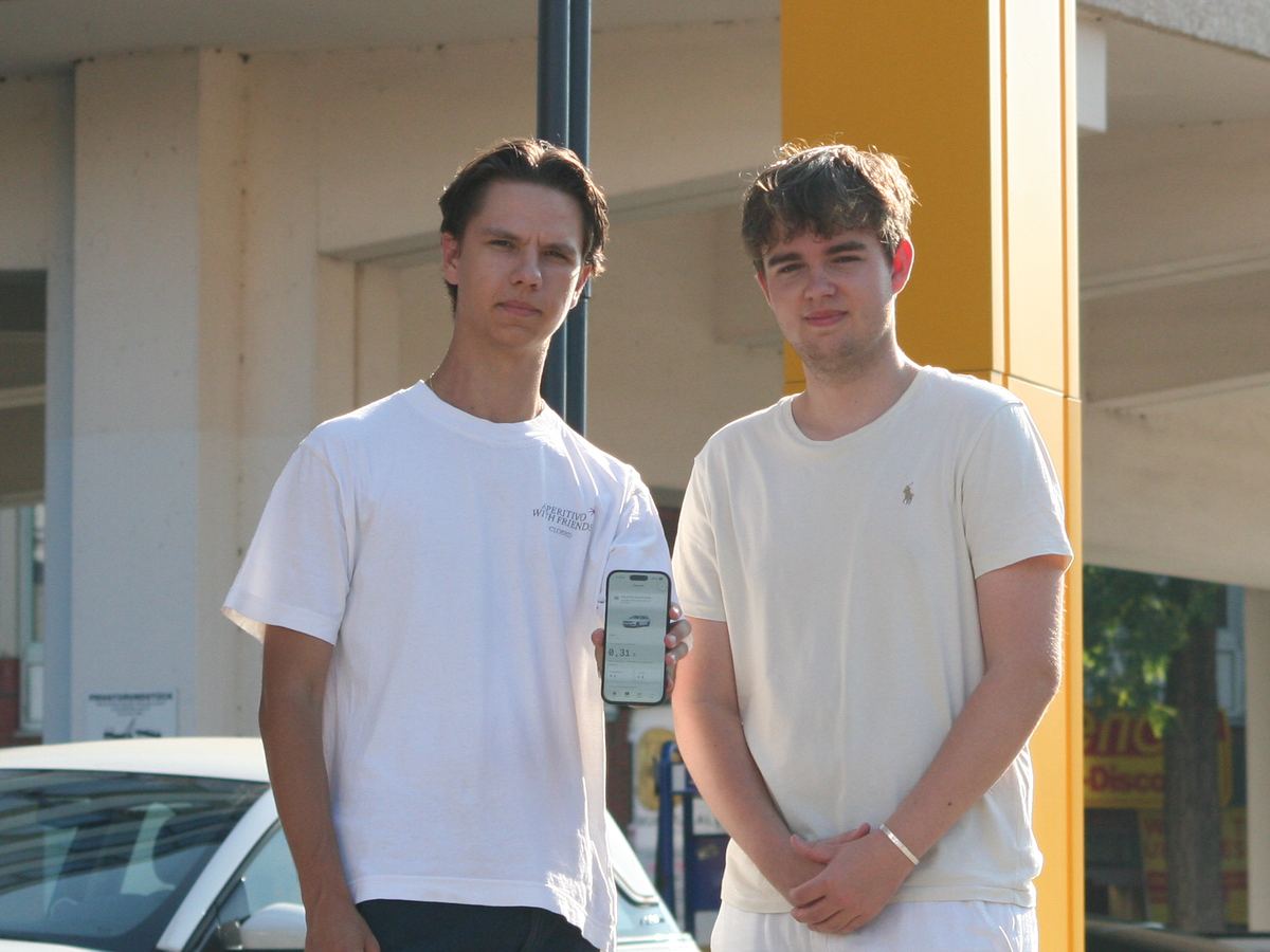 Florian Ritzel und Jannik Kirchhoff, die beiden Gründer von Marlow, an einer Tankstelle in Hamburg. Einer von beiden hält ein iPhone mit den echten Kosten je Kilometer in der App.